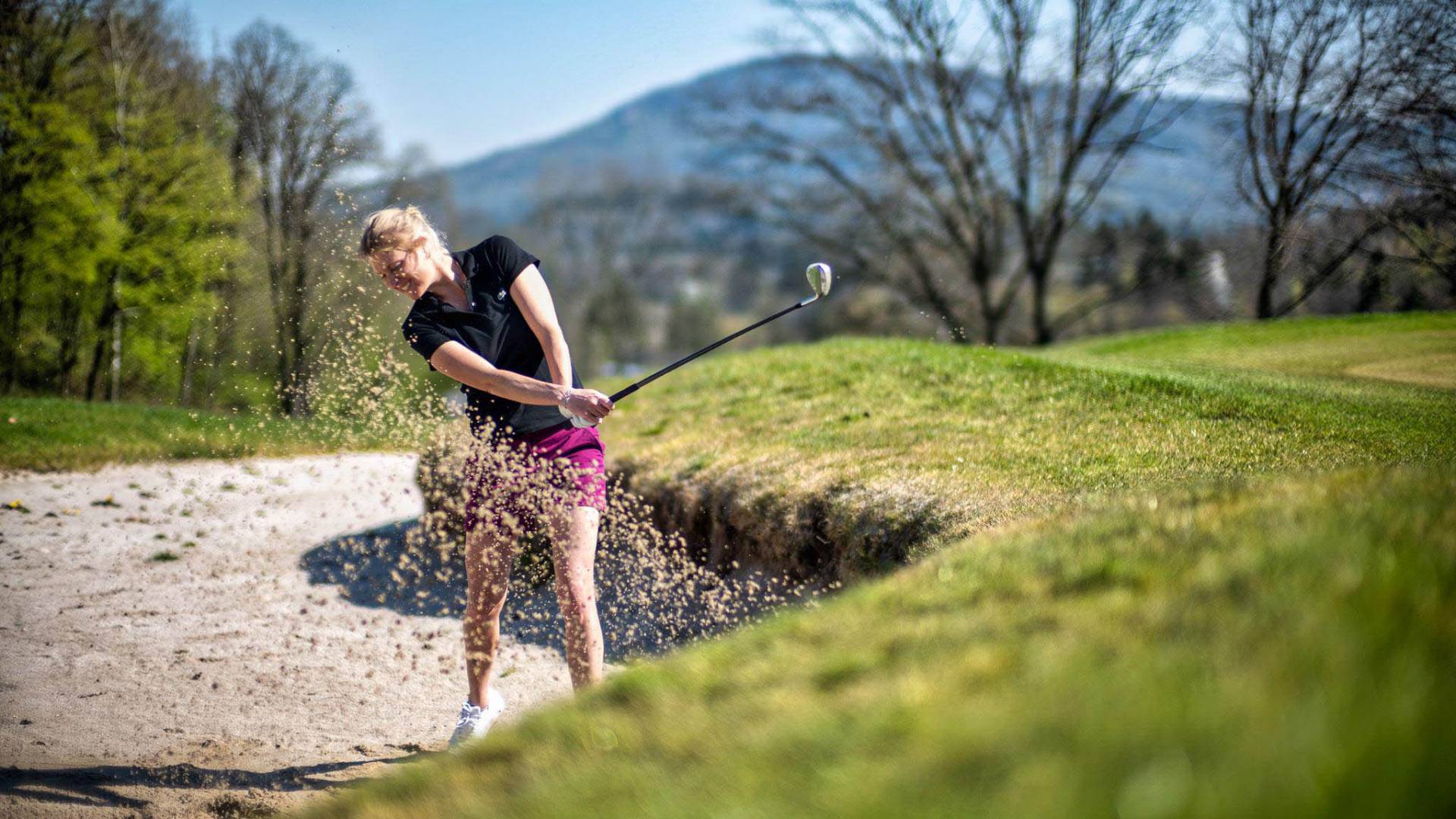 Golferin beim Abschlag im Sand